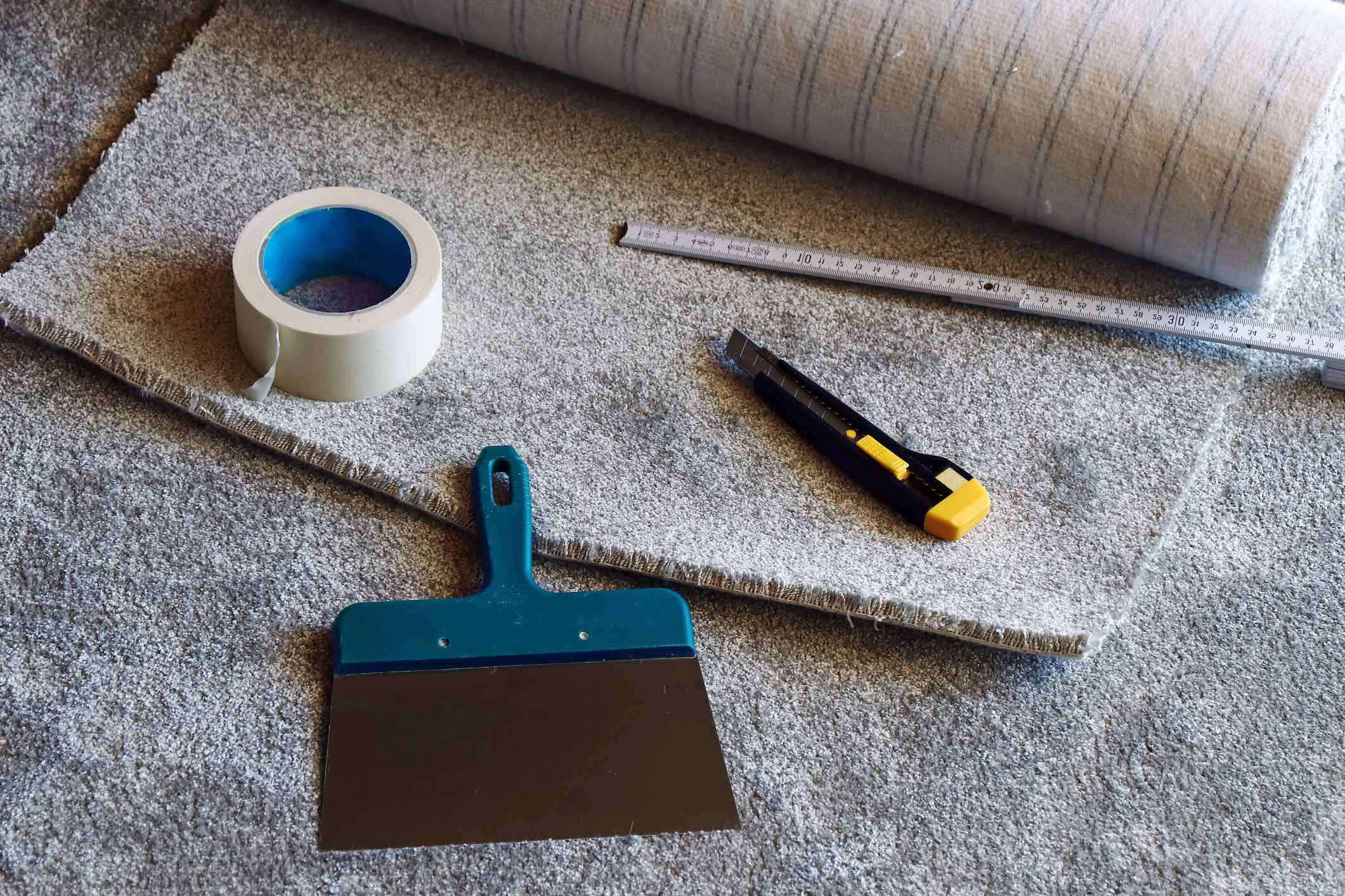 Professional carpet installation tools including utility knife, tape, trowel, and rolled carpet — expert carpet replacement and repair services in Orange County.