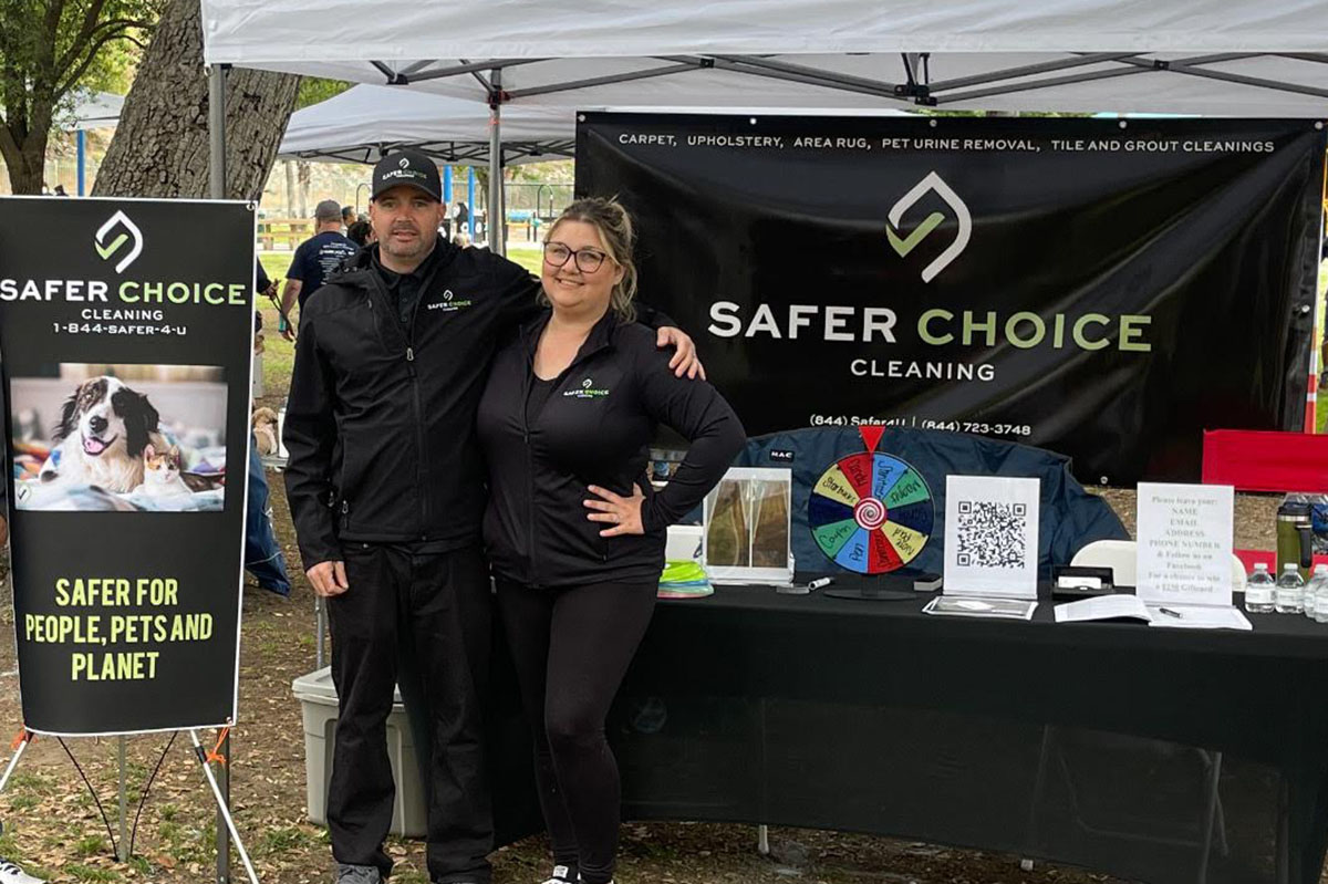 Mike Leffler, owner of Safer Choice Cleaning, standing with his wife Andrea at local community event booth—promoting eco-friendly carpet, upholstery, and pet urine removal services in Southern California.